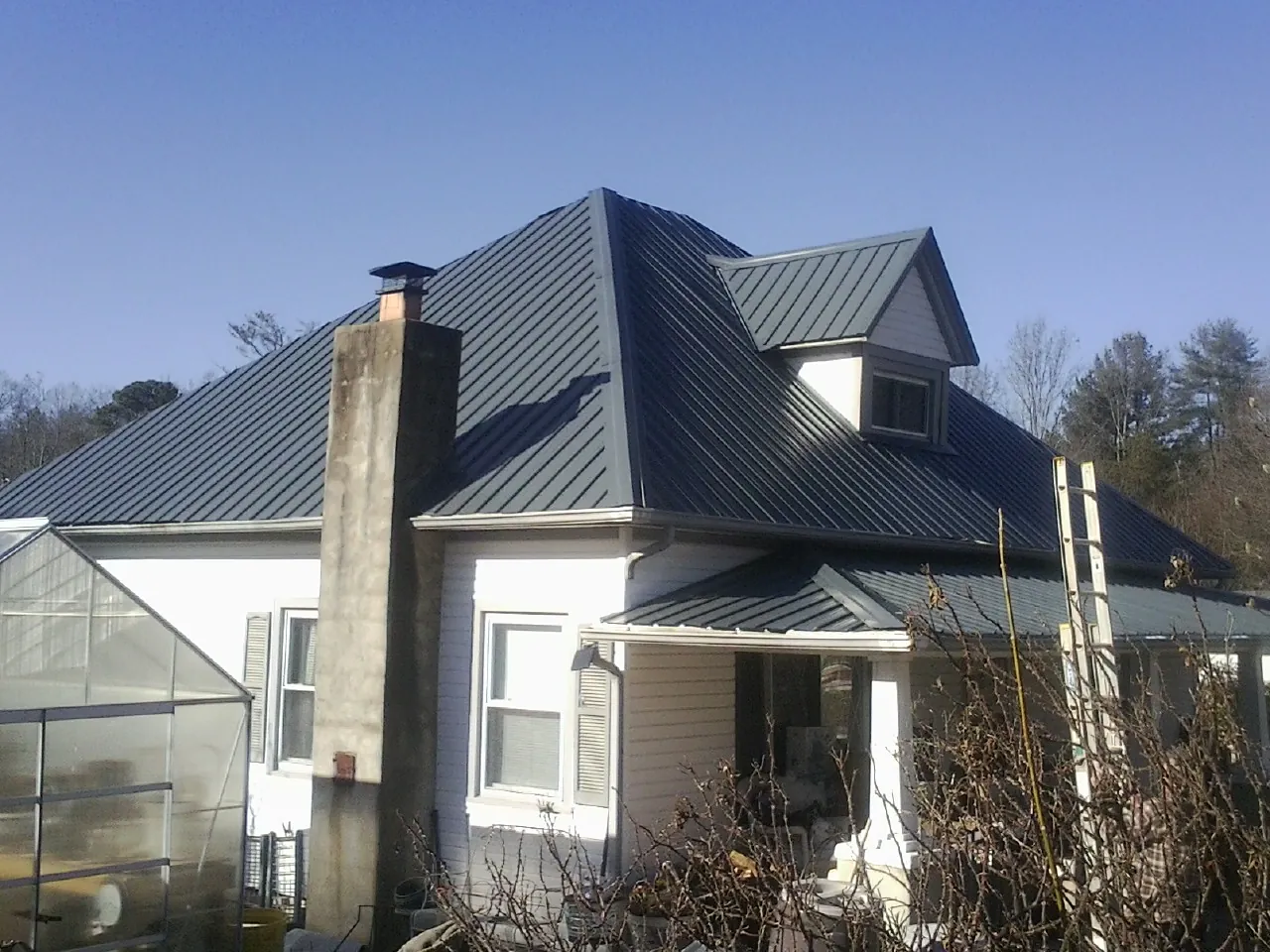 Dark blue standing seam metal roof on a white farmhouse with dormer — Slate & Tile Roof Repair by Roofing Brothers in Salina