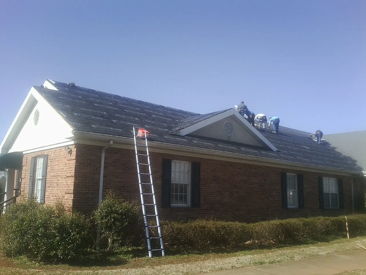 Crew tearing shingles off a brick ranch roof with a ladder set — Emergency Roof Repair work by our crew in Salina