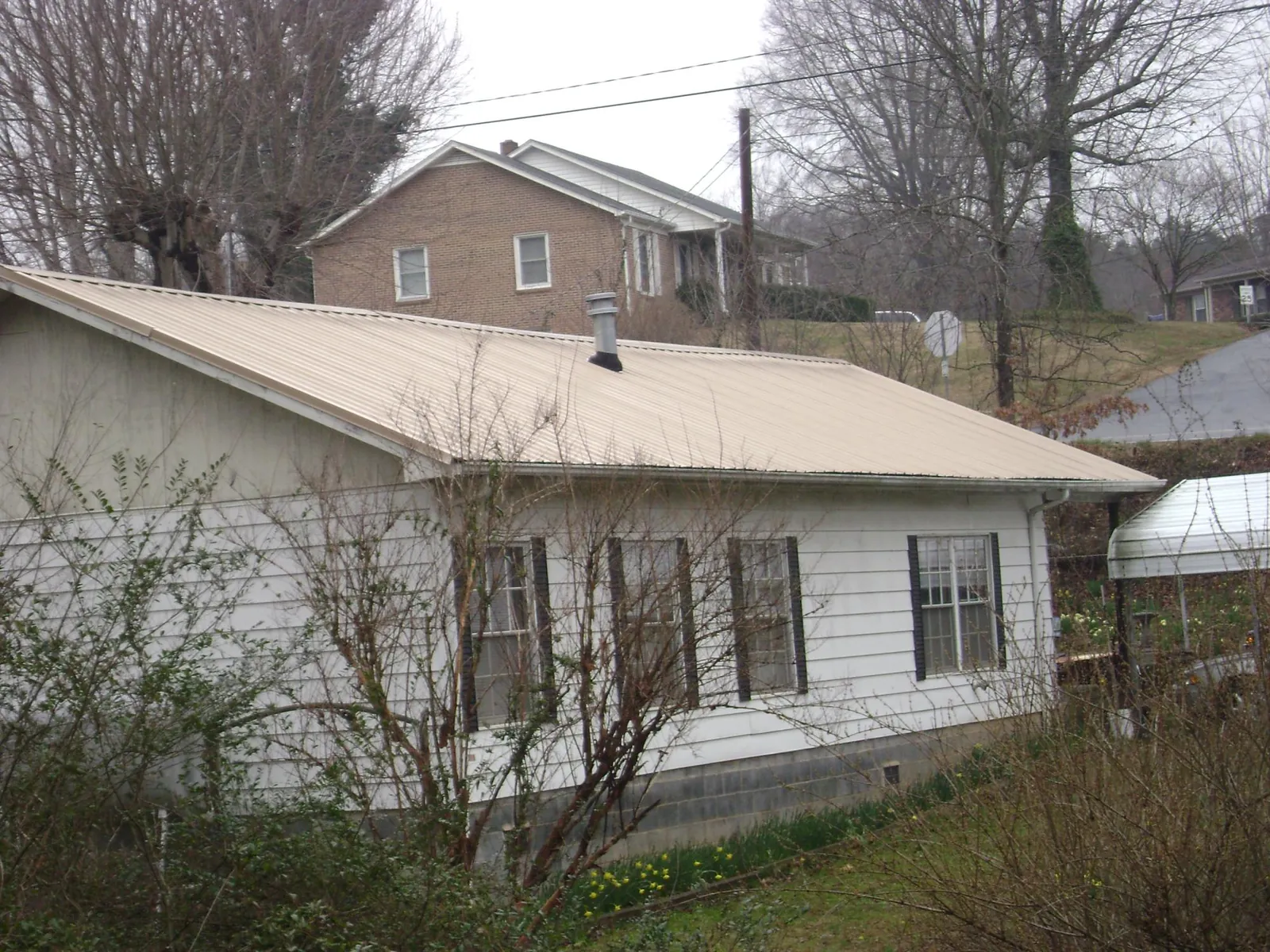 Tan metal roof on a white sided house set into a hillside — Commercial Roofing by Roofing Brothers in Salina