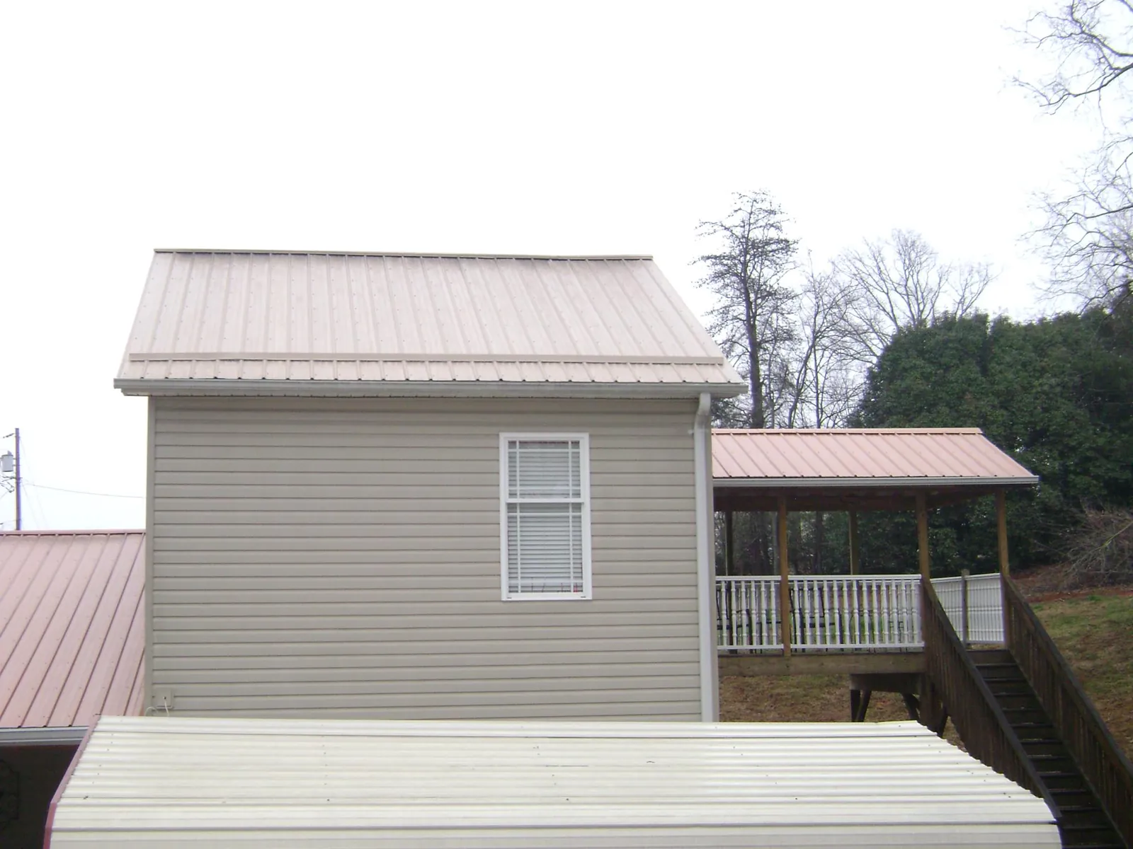 Tan metal roofs on a two story addition and attached porch, from a Roof Replacement job in Salina
